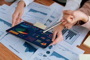 Two professionals reviewing financial reports and charts on a tablet displaying business analytics and performance data.